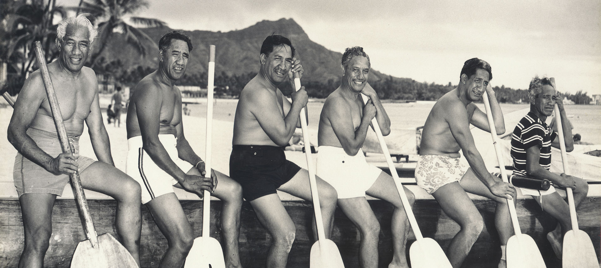 Duke and men sitting lined up by the shore with oars