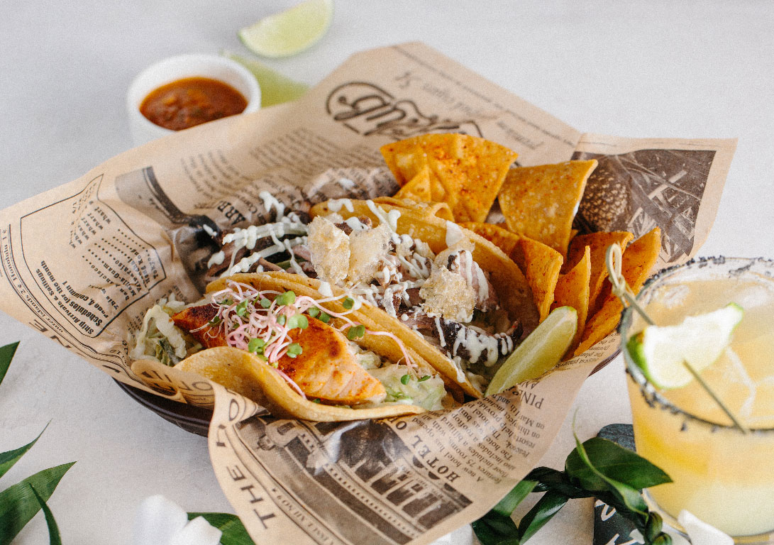 photo of a plate of tacos with salsa, cocktail, and limes